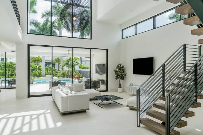 Double-height white living room opening onto a palm-lined pool terrace