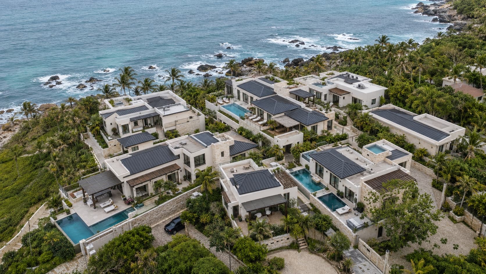 Aerial view of a completed 2Can Homes oceanfront villa development, pools and palm-lined terraces along the rocky coastline