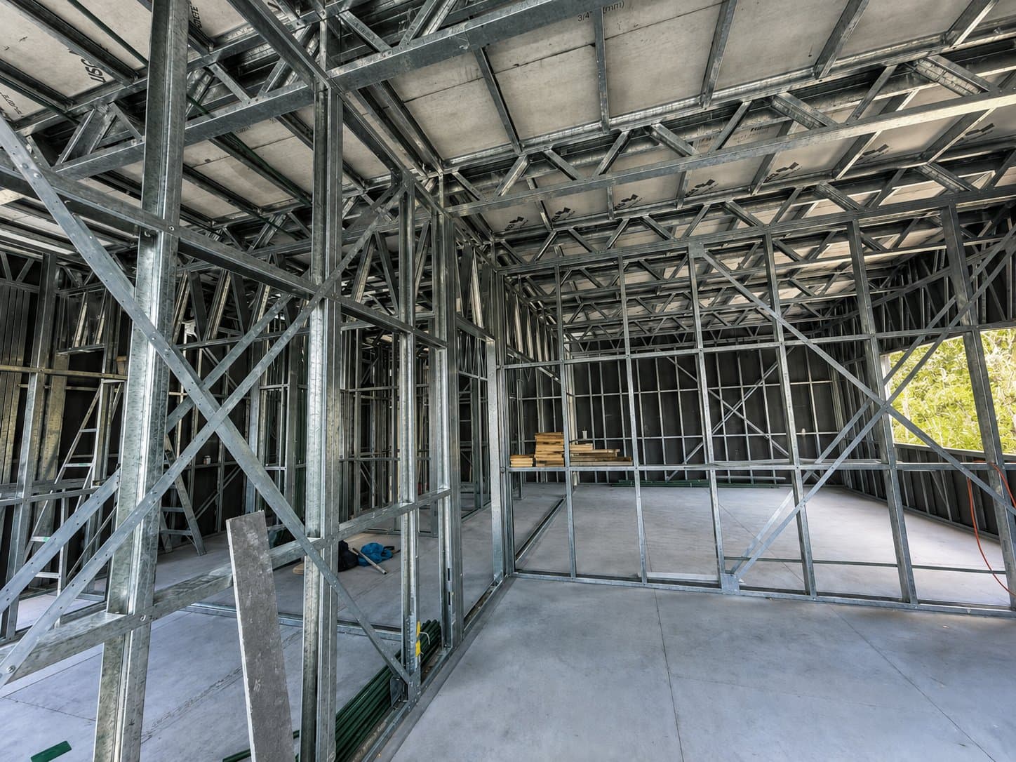 A galvanised steel house frame mid-build at golden hour, finished residences beyond