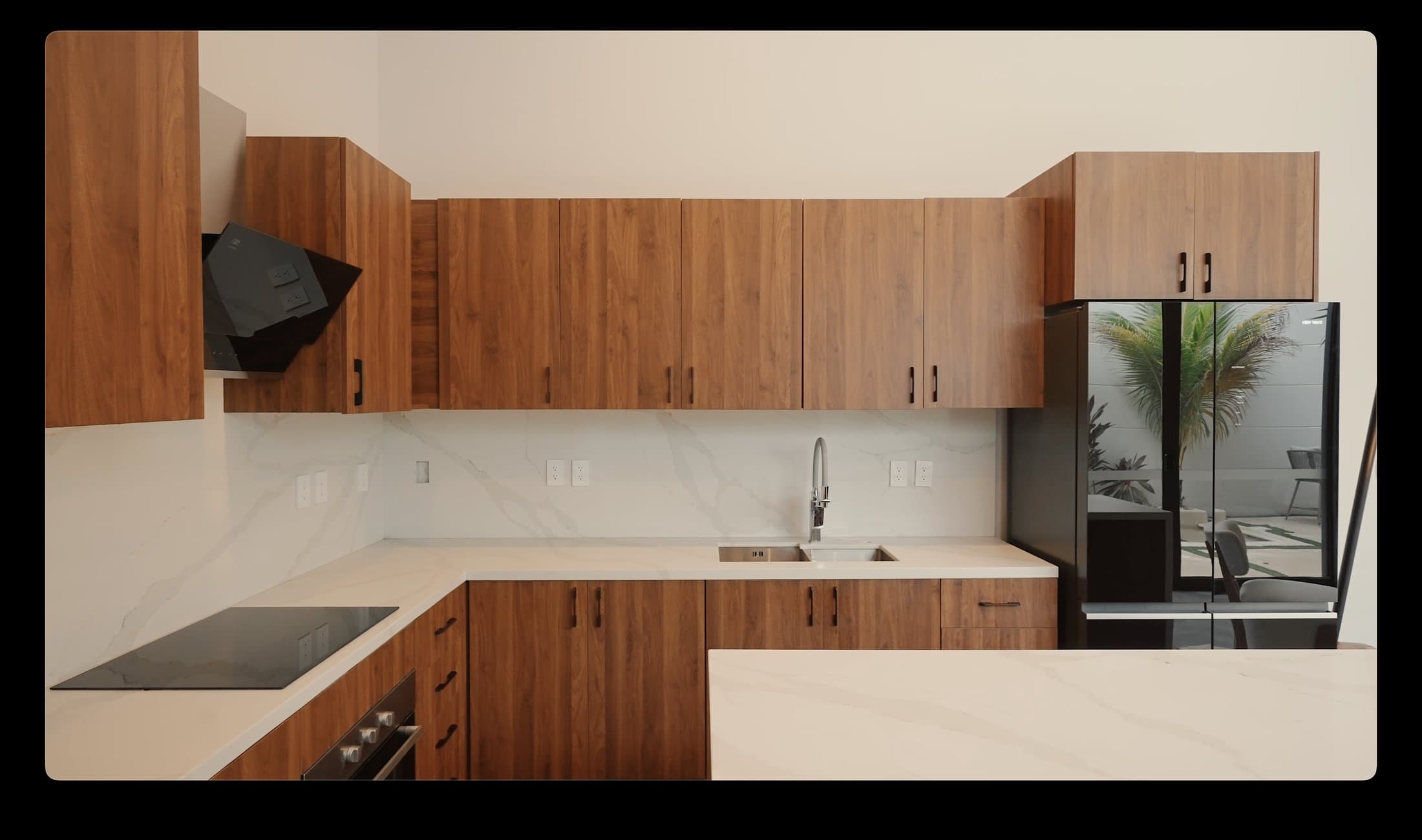 Walnut kitchen cabinetry with marble backsplash and a garden view through the fridge's glass panel